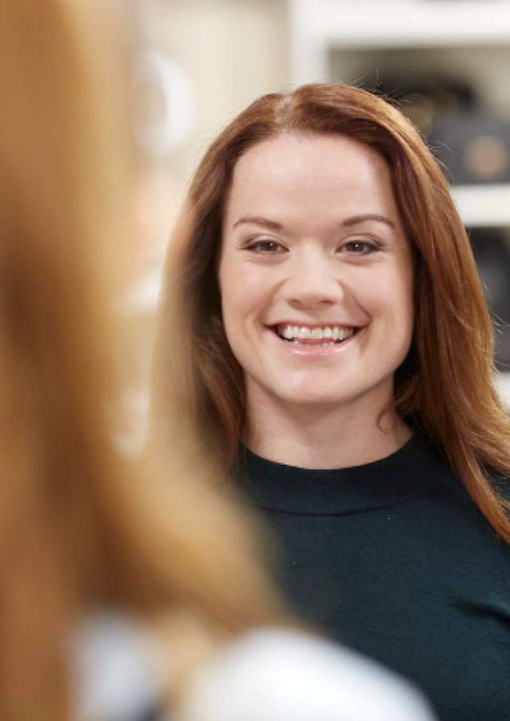 Kvinne med rødt hår smiler og ser i speil på badet.