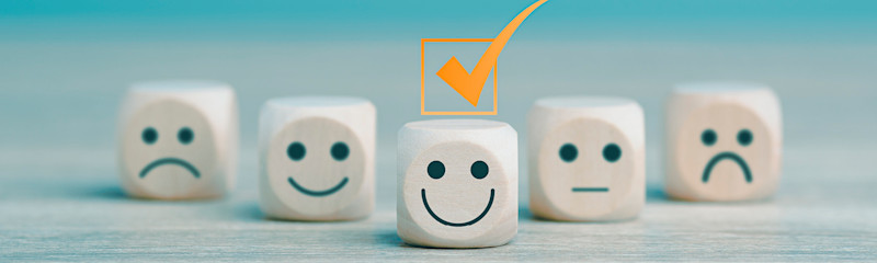 Tre terninger med ansikter som viser trist, nøytral og glad, hvor den glade terningen i midten er merket med en oransje hake.