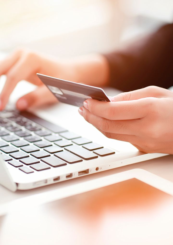 Hånd holder et kredittkort og taster på en bærbar datamaskin i et lyst miljø.