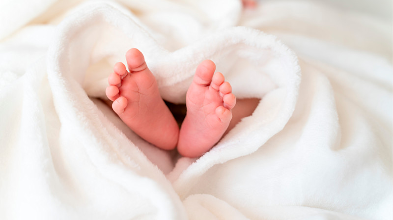 Nyfødte babyføtter som stikker ut fra et mykt, hvitt teppe formet som et hjerte.